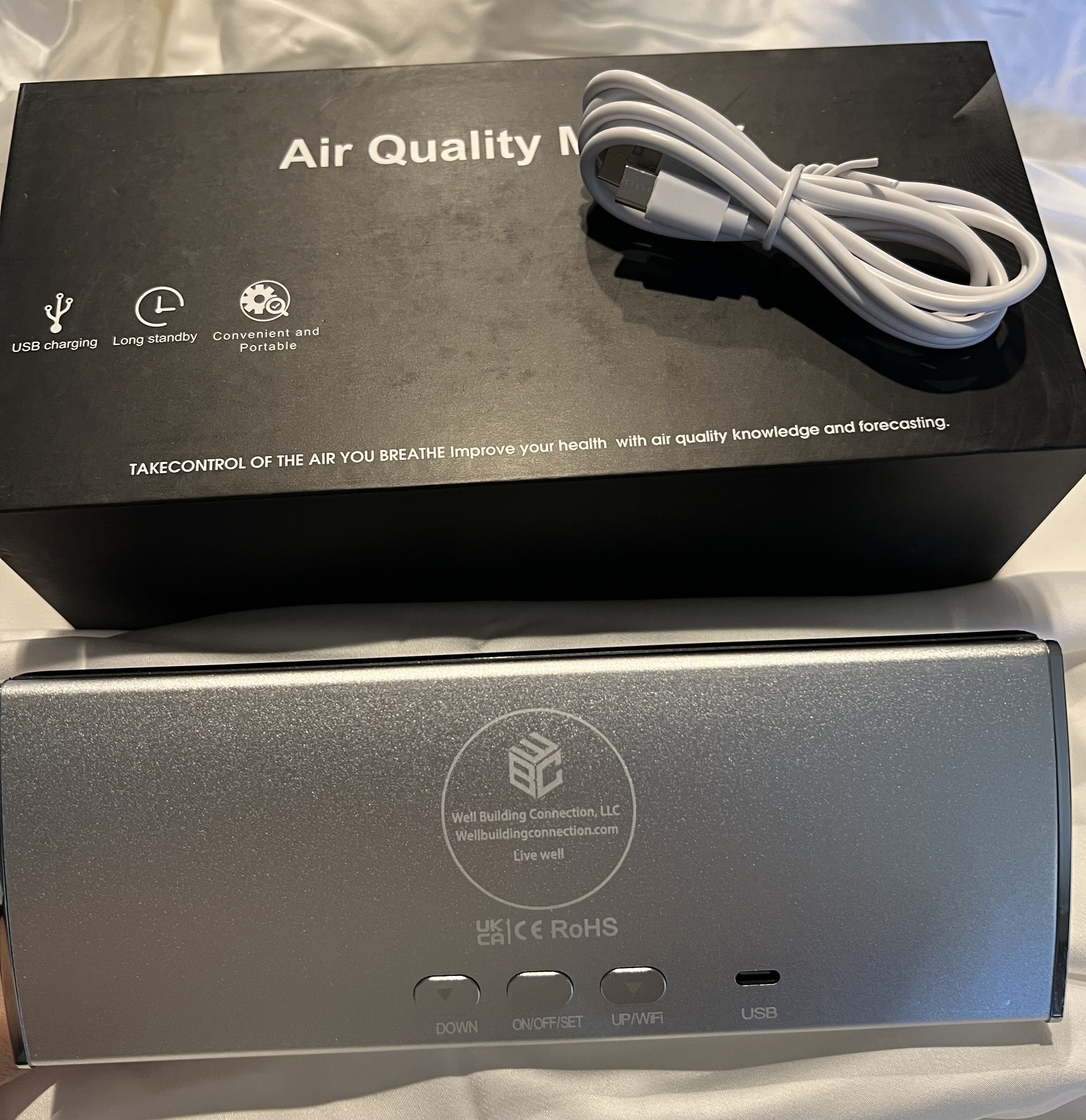 Digital 9 in 1 air quality monitor with various readings on a white background. pm 2.5, CO2, and Radon Monitoring. USB Cable on black box. Monitor your IAQA at home or in the workplace with this portable device.