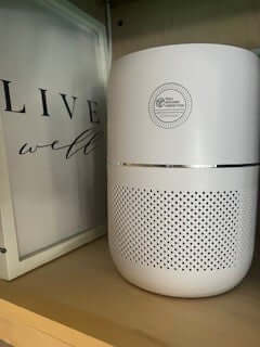 White Hepa Air Purifier. A white cylindrical HEPA air purifier with a perforated lower section and a Well Building Connection logo on the front. Indoor Air Pollutants too many to list and everyone benefits from this air purifier from Well Building Connection.
