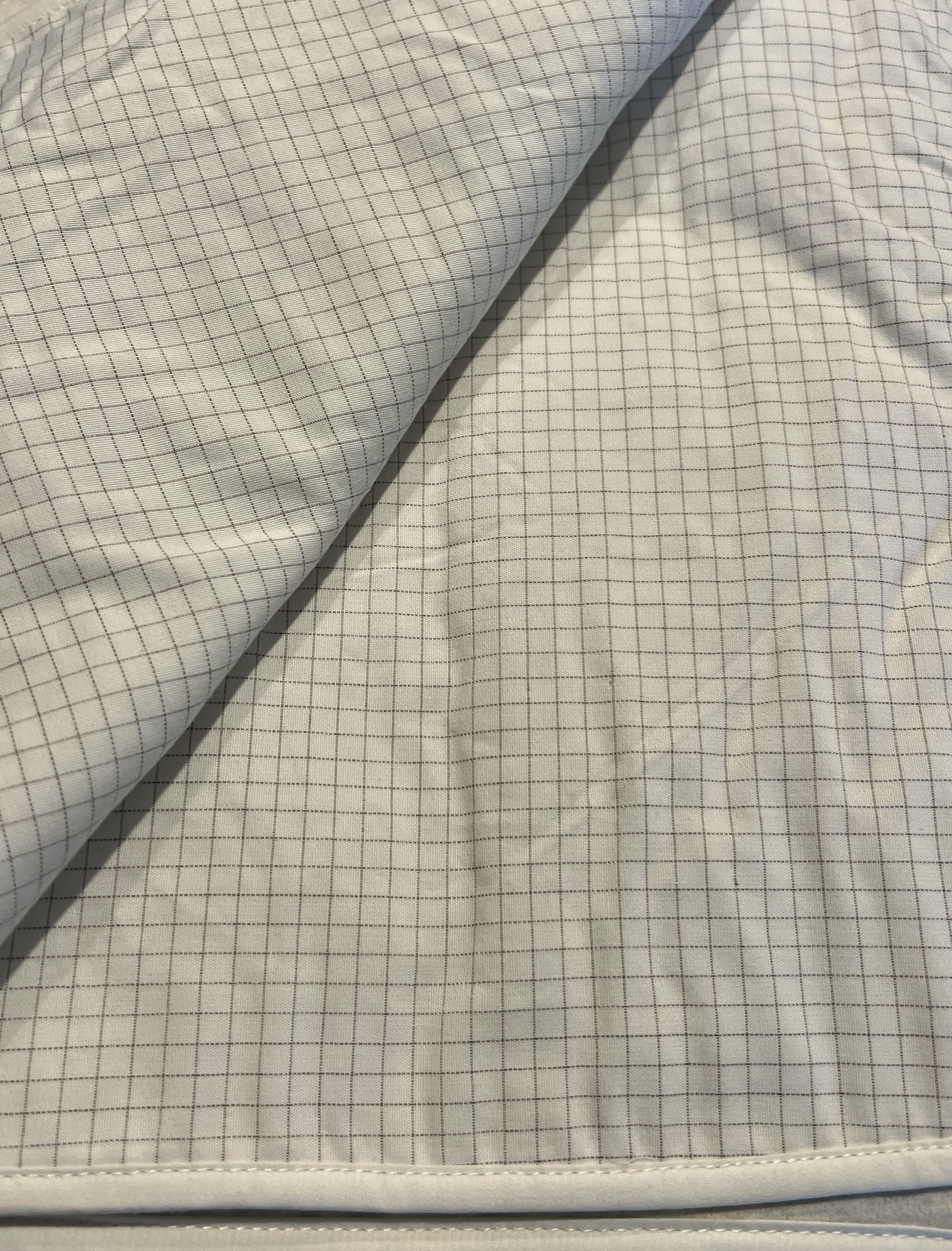 Close-up of a textured fabric with silver-threaded grounding blanket grid pattern on grounded blanket. 