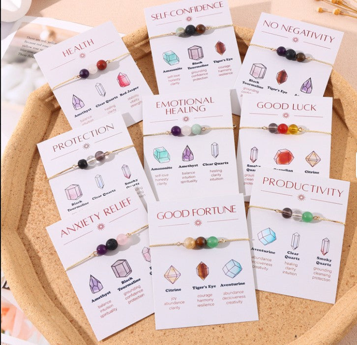 Set of crystal bracelets with corresponding cards on a wooden surface. Self-Care and Well-being: Gifting yourself or wearing intentional jewelry can enhance your mood, increase feelings of joy, and contribute to overall emotional well-being.